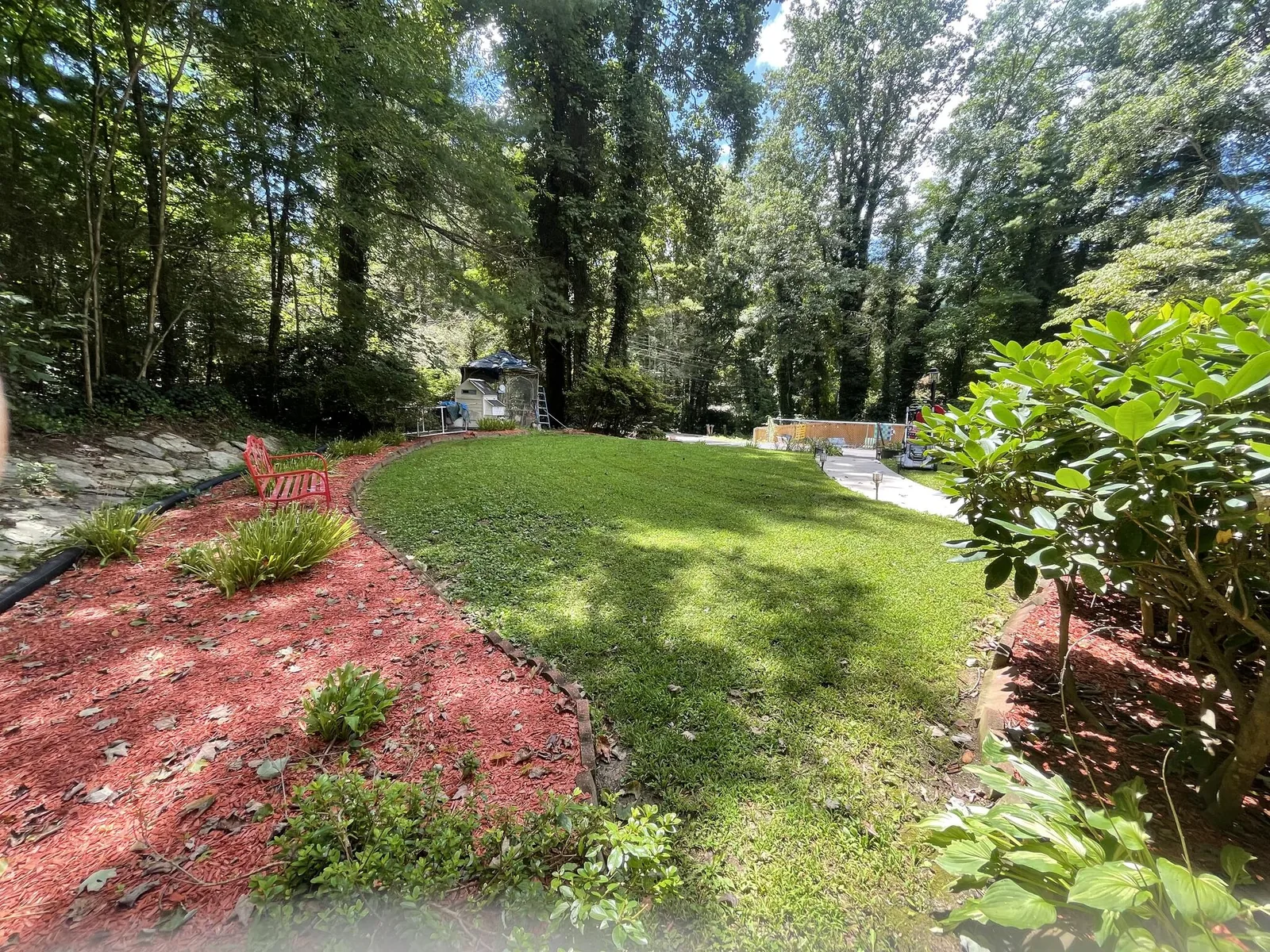Fresh red-dyed mulch beds curving around a cut lawn on a wooded lot